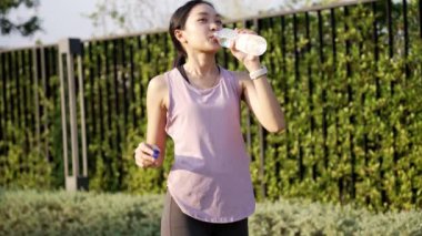 Genç jimnastikçi kadın parkta gerinirken enerji suyu içiyor. ve akşamları egzersiz, sağlık konsepti yavaş çekim videosu