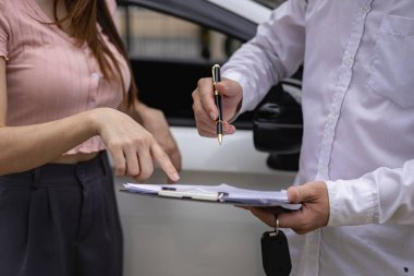 Sigorta çalışanı, trafik kazası ve sigorta kavramının ardından hasar gören araba ve müşteri imzalarını kontrol ediyor.