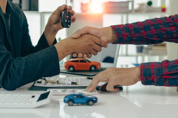 The dealer hands the car keys to the new owner. Sales, loan, finance, car rental, insurance, dealer, installment, car care business. Businessman shaking hands with keys to customer in office,