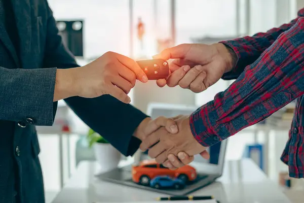 The dealer hands the car keys to the new owner. Sales, loan, finance, car rental, insurance, dealer, installment, car care business. Businessman shaking hands with keys to customer in office,