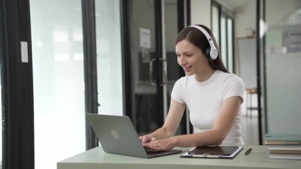 ノートパソコンでインターネットを勉強しているヘッドフォンのGen Zの若い学生少女 オーディオナレーションに耳を傾ける Webinars Writingノート オンラインポッドキャストを聞く リスニングトレーニングコースを受講している女性 — ストック動画
