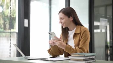 Uzak kariyer. Cep telefonuyla konuşan ve evde dizüstü bilgisayar kullanan gülümseyen bir kadın. Ev bilgisayarında çalışırken cep telefonu kullanan genç serbest çalışan bir kadın. Yüksek kalite 4k görüntü