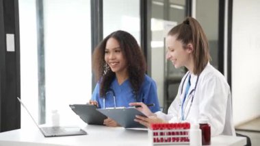 İki kadın doktor virüs testi için kan örnekleriyle test tüplerini inceliyor. Virüs salgınından kalma koruyucu eldivenler, sağlık ve güvenlik konsepti giyiyorlar..