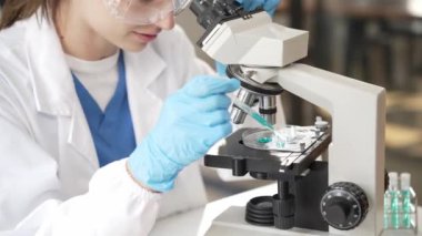 Biyoteknoloji bilim adamlarından oluşan bir ekip deney tüplerini bir araştırma laboratuarında deney yapmak için kullanıyor. Kadın araştırma mikroskobu ve laboratuvarda bilim adamının laptopunu kullanan iki kişi.