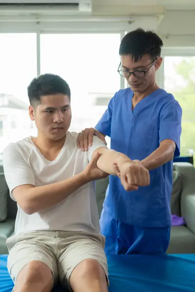 Physiotherapy doctor treating patient whose arm is recovering, doing physical therapy to stretch muscles in clinic