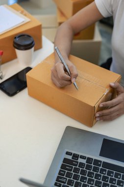Evden çalışan Asyalı kadın KOBİ girişimcileri ticari izleme için akıllı telefon ve dizüstü bilgisayar kullanıyorlar. Çevrimiçi pazarlama bir paket kutusunda paketlenmiş. Resmi kapat.