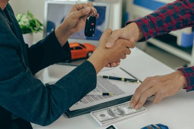 Adam araba alır ve iş adamı ile el sıkışır, araba satış anlaşmasını kapatır, jest ve konsept olarak yeni sahibine anahtar verir ve araba fuarında yakın çekim fotoğraflarında el sıkışır.