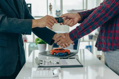 Adam araba alır ve iş adamı ile el sıkışır, araba satış anlaşmasını kapatır, jest ve konsept olarak yeni sahibine anahtar verir ve araba fuarında yakın çekim fotoğraflarında el sıkışır.