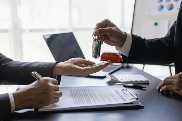 Car dealer hands keys to customer, closing car insurance documents or rental agreement or agreement. Buying or selling a new car, close-up photo