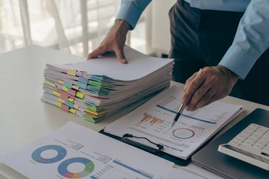 İş adamının elinde masasında ev ofisiyle ilgili bilgi aramak için bir yığın kağıt var. İş raporu. Masanın üzerinde bitmemiş bir yığın belge var..