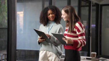 İşteki yeni bir projeyle ilgili toplantıda, iki genç kadın raporlara bakarken ve dizüstü bilgisayar ve tabletleri birlikte kullanırken konuşuyor ve ciddi görünüyor. 4k 60p