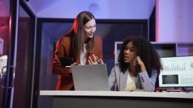 Laptop ve tablet kullanarak birlikte çalışan iki iş kadını masada oturup yeni projeyi tartışıyor. Afrikalı Amerikalı kadın ve sarışın kadının 4K 60p numaralı ofiste buluşması gibi yaratıcı bir kavram.