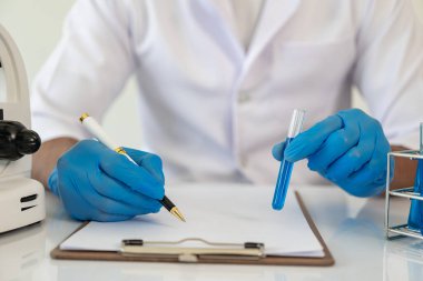 Laboratuvar konsepti: Laboratuvarda kimyasallara yakın çekim yapan bir biyokimyager, laboratuvarda kontrollü bir ortamda deneyler yapıyor. Doktor eldiven giymiş, elinde test tüpü tutuyor.