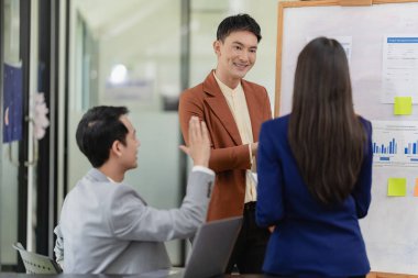 Takım elbiseli Asyalı başarılı iş adamlarından oluşan bir ekip beyin fırtınası, hesaplama, analiz ve şirket büyüme hedefleri ve brüt kâr marjlarını tartışmak için konferans odasında çalışıyor..