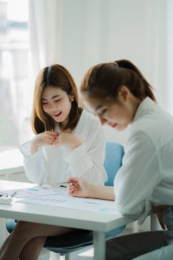 İki Asyalı kadın muhasebeci iş ofisindeki finansal bilgileri özetlemek için takım toplantısı yapıyorlar. Yaratıcı kadın yönetici tableti kullanıyor ve gülümsüyor.