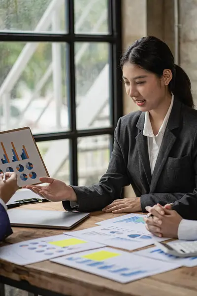 Young professional Asian accountant or financial analyst presents a financial report during a financial business sales data meeting with her colleagues in the office.