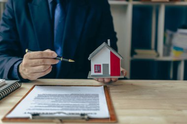 Bir emlakçı müşterileri tanıtmak için küçük bir ev modeli tutuyor. Model ev projesi ve müşterilere anahtar verilmesi konut kredisi ve sigorta sözleşmesi için yeni alıcılar onaylanır.