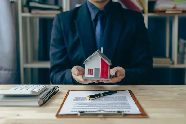A real estate salesperson holds a small house model to introduce customers. Model house project and give keys to customers New home buyers get approved for a home loan and insurance contract.