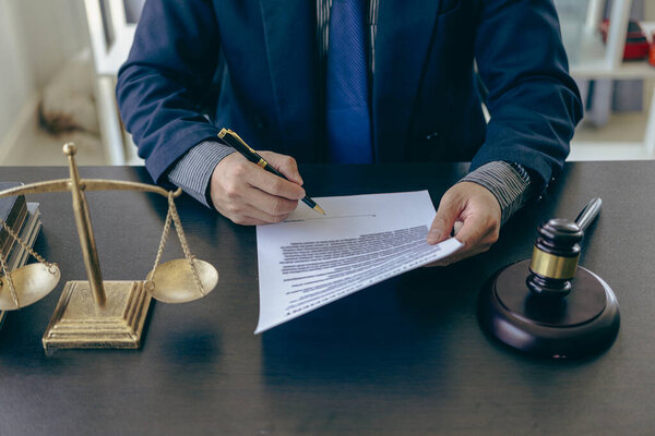 Close-up shot of lawyer working with contract documents and hammer on scales of justice, legal consultant concept.