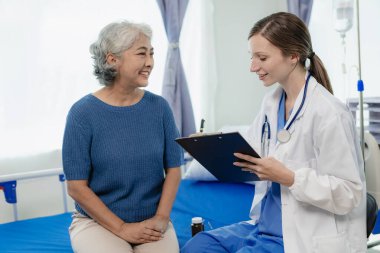 Kadın bir doktor test sonuçlarına bakarken yaşlı bir kadın hastayla konuşur. Bir hasta, kadın bir doktora tedavi ve sağlık tavsiyesi hakkında danışmaktadır..