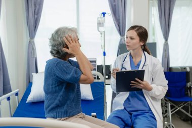 Kadın bir doktor test sonuçlarına bakarken yaşlı bir kadın hastayla konuşur. Bir hasta, kadın bir doktora tedavi ve sağlık tavsiyesi hakkında danışmaktadır..