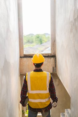 Genç adam mühendis ya da inşaat denetçisi proje üzerinde çalışıyor, miğfer ve yelek giyen mimar teftiş ve teftiş yapıyor. Yapılan iş kalitesi
