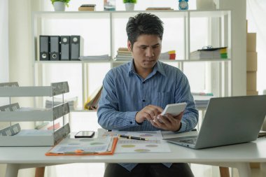 Home Man 'de çalışan yakışıklı Asyalı işadamı bilgisayarla iş yerinde performans analizi raporu hazırlayan dizüstü bilgisayarlı grafikleri ve çizelgeleri analiz ediyor..