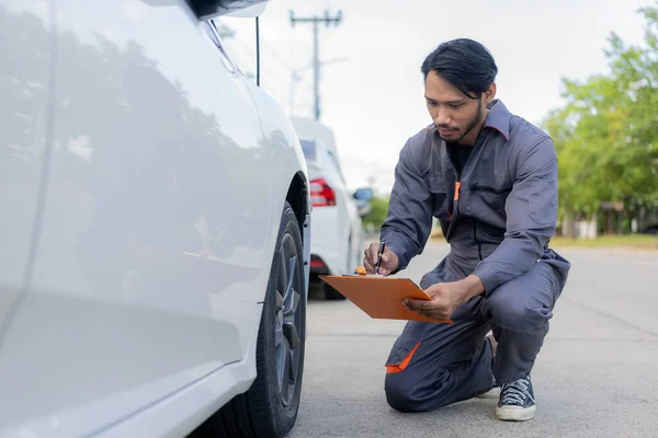 maintenance concept Asian auto mechanic or smith writing on clipboard at warehouse workshop Technician making checklist for car repair Roadside breakdown and insurance concept