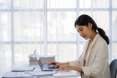 Ofiste dizüstü bilgisayarla çalışan neşeli Asyalı kadın, resmi takım elbiseli mutlu, ofiste çalışan, gülümseyen kadın ofis çalışanı, finansal muhasebe kavramı