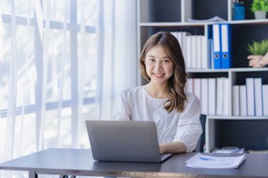 Ofiste dizüstü bilgisayarla çalışan neşeli Asyalı kadın, resmi takım elbiseli mutlu, ofiste çalışan, gülümseyen kadın ofis çalışanı, finansal muhasebe kavramı