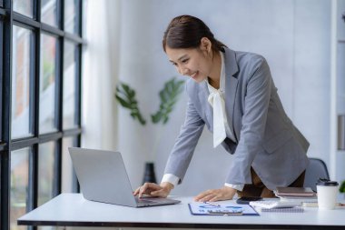 Ofiste dizüstü bilgisayarla çalışan neşeli Asyalı kadın, resmi takım elbiseli mutlu, ofiste çalışan, gülümseyen kadın ofis çalışanı, finansal muhasebe kavramı