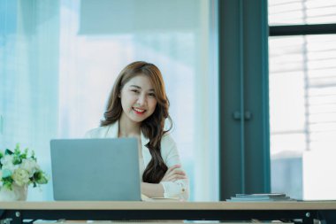 Ofiste dizüstü bilgisayarla çalışan neşeli Asyalı kadın, resmi takım elbiseli mutlu, ofiste çalışan, gülümseyen kadın ofis çalışanı, finansal muhasebe kavramı