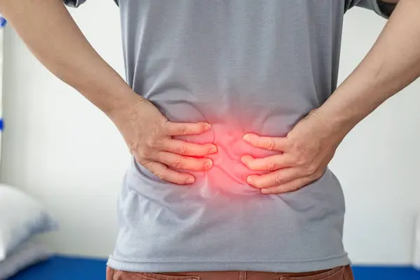 Office Syndrome: Man touching lower back at pain point with red notes, back and waist pain. Asian man touching back with musculoskeletal pain. Close-up photo
