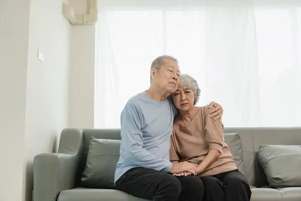 Asian senior couple looking at camera and smiling, senior smiling and looking at tablet Retired people use technology at home Woman hugging man with love Together forever on the sofa at home