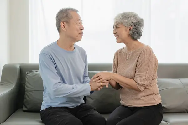 Asian senior couple looking at camera and smiling, senior smiling and looking at tablet Retired people use technology at home Woman hugging man with love Together forever on the sofa at home