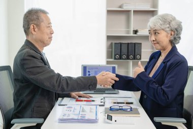 İki kıdemli Asyalı iş adamı, yönetim toplantısı ve iş ortaklığı konsepti anlaşmasında el sıkışan erkek ve kadın. İki işadamı anlaşma yaptıktan sonra el sıkışıyor..