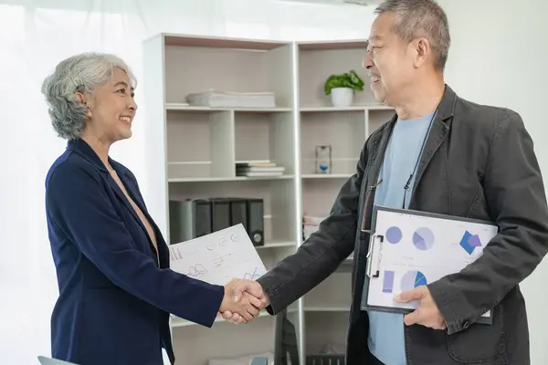 Two senior Asian businessmen, man and woman shaking hands during management meeting and agreement in business partnership concept. Two businessmen shake hands after making a deal.