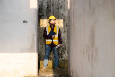 Mimarlık şantiyesinde güvenlik yeleği ve kask giyen Asyalı inşaat yöneticisi inşaat alanında beyaz şapkalı bir erkek inşaat denetçisi inşaat alanını teftiş ediyor..