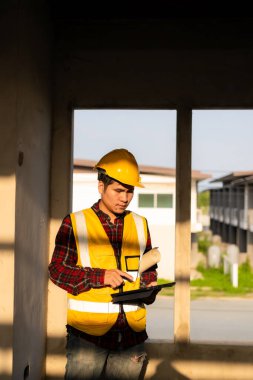Mimarlık şantiyesinde güvenlik yeleği ve kask giyen Asyalı inşaat yöneticisi inşaat alanında beyaz şapkalı bir erkek inşaat denetçisi inşaat alanını teftiş ediyor..