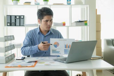 Profesyonel Asyalı erkek satıcı ev ofisinden gelen dizüstü bilgisayarla müşterilere kâğıt belgeler sunuyor..