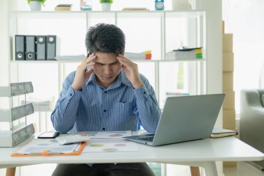 Başı ağrıyan iş adamı kavramı ofiste dizüstü bilgisayarı kafasına değen bir masada stresli bir şekilde oturuyor. Girişimciler işleriyle ilgili sorunlarla karşı karşıya.