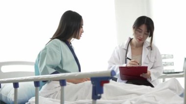 Hastane yatağında yatan bir hastanın yatağında yatan kadın hastayı muayene eden üniformalı bir Asyalı kadın doktor.