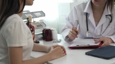 Beyaz üniformalı Asyalı kadın doktor, kadın hastalarla sonuçları ya da belirtileri tartışıyor ve klinikteki kadın müşterilere tavsiyelerde bulunuyor..