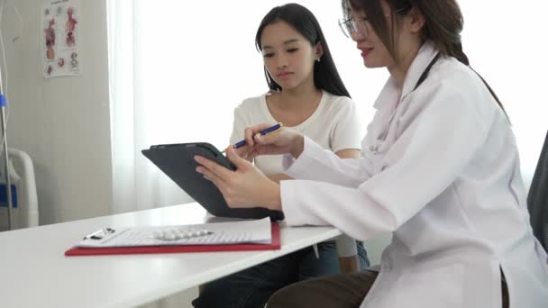白い医療服のアジアの女性医師は 女性患者との結果や症状を議論し クリニックの女性顧客にアドバイスします — ストック動画