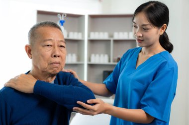 Yaşlı bir Asyalı, bakıcısıyla birlikte bir hasta için egzersiz yaparak oturma odasındaki hemşirenin desteğiyle fiziksel terapi yapıyor. Yaşlılar için fizik tedavi