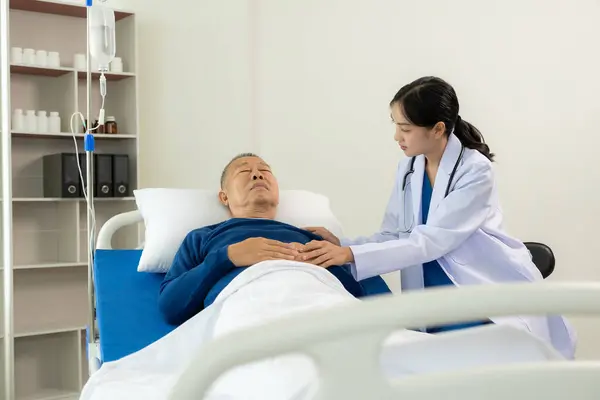An old man hospitalized lies in bed while a doctor checks his pulse. Doctor or nurse examining a senior male patient, caring for and encouraging him in the hospital room, lying on the bed.
