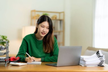 Evden çalışan hırslı Asyalı kız dizüstü bilgisayar ekranına bakıyor, gülümsüyor, e-postaları kontrol ediyor ya da uzaktan araştırma yapıyor.