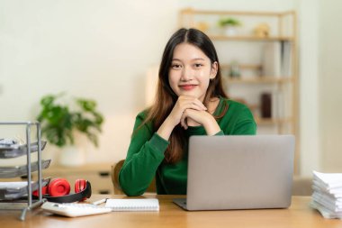 Evden çalışan hırslı Asyalı kız dizüstü bilgisayar ekranına bakıyor, gülümsüyor, e-postaları kontrol ediyor ya da uzaktan araştırma yapıyor.