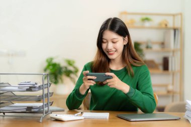 Evden çalışan hırslı Asyalı kız dizüstü bilgisayar ekranına bakıyor, gülümsüyor, e-postaları kontrol ediyor ya da uzaktan araştırma yapıyor.