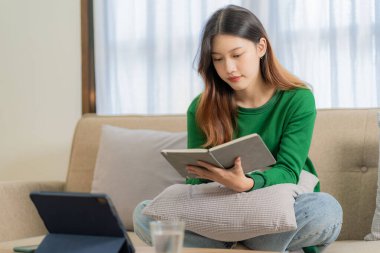 Evden çalışan hırslı Asyalı kız dizüstü bilgisayar ekranına bakıyor, gülümsüyor, e-postaları kontrol ediyor ya da uzaktan araştırma yapıyor.